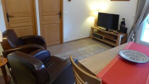 A living room with a TV, two leather chairs, a wooden table, and a red table runner.