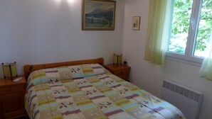 A bedroom with a bed, bedside tables, a window with curtains, a radiator, and a painting on the wall.