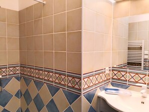 Een badkamer met betegelde vloer, een wastafel, een spiegel en een handdoekrek.