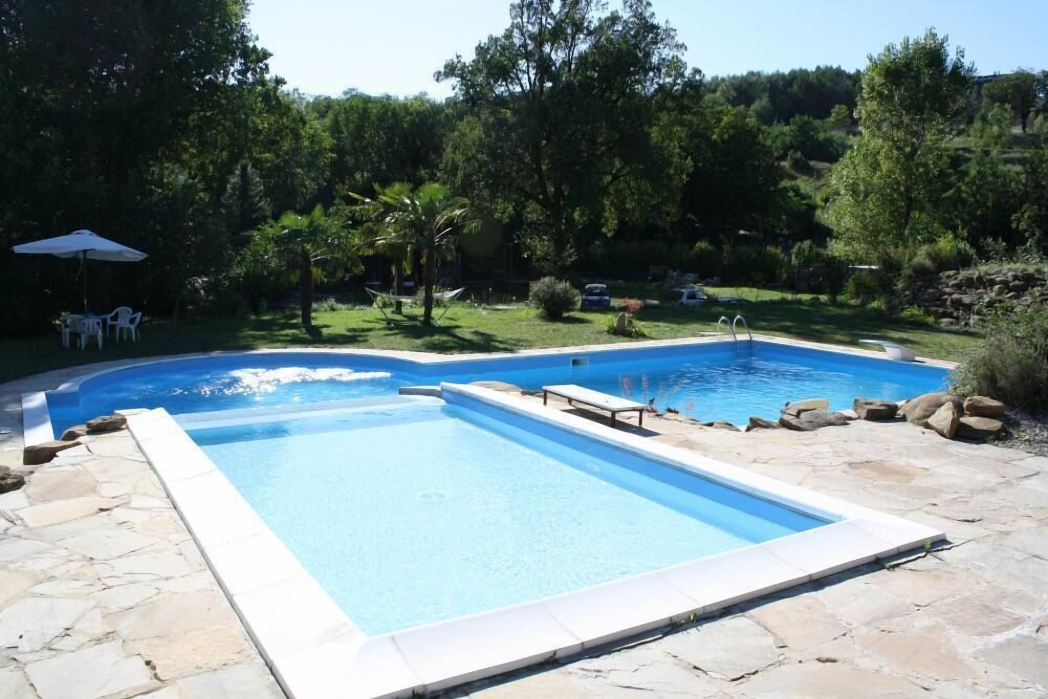 Piscina retangular com borda de pedra, rodeada por um pátio de pedra.