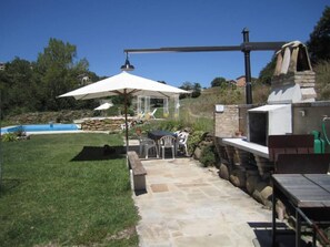 Une terrasse avec un sol en pierre, un barbecue et une piscine.
