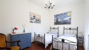 A bedroom with two beds, a dresser, a chair, and artwork on the walls.