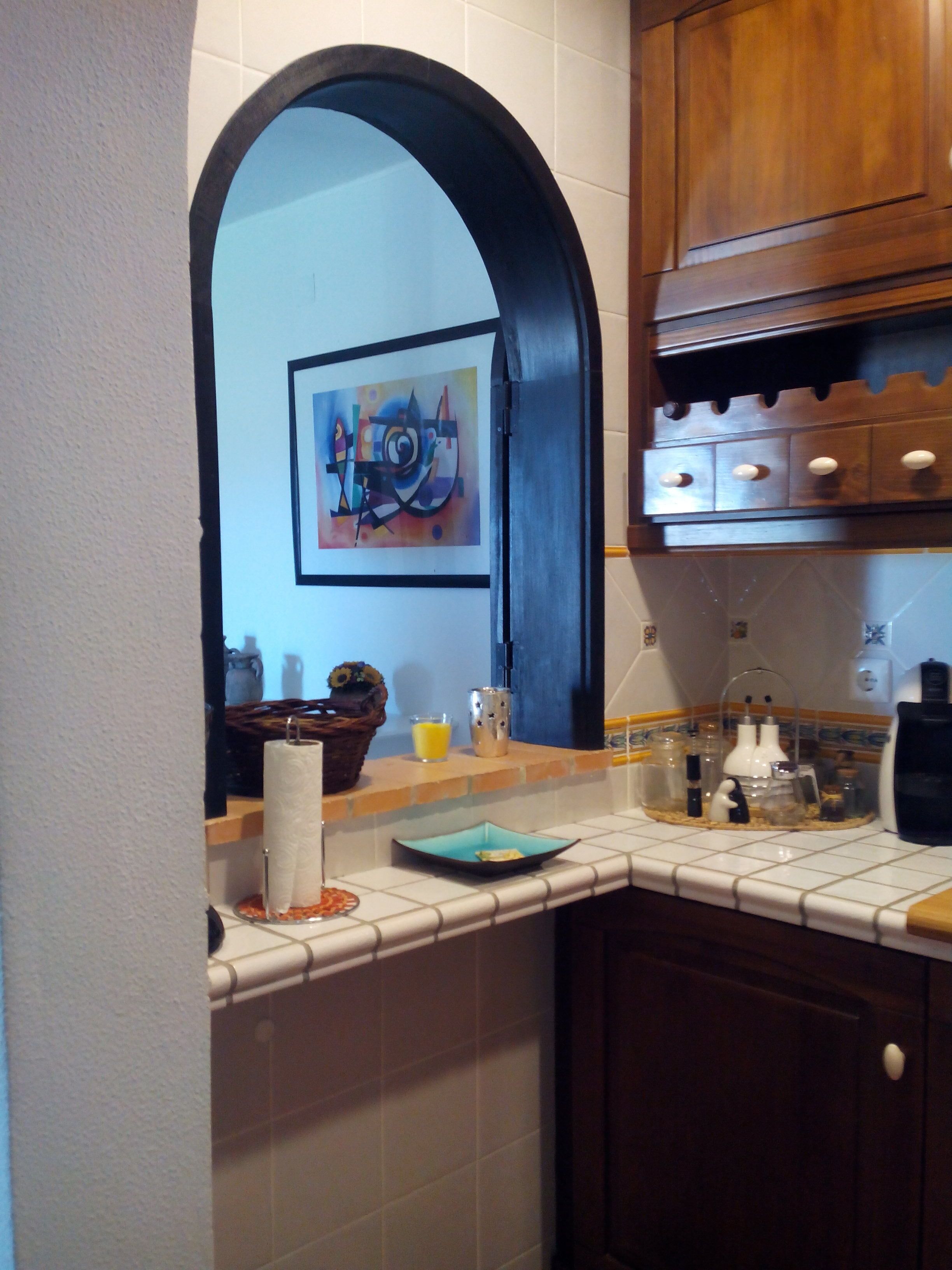 A kitchen with white tiles, a wooden cabinet, and a framed artwork on the wall.