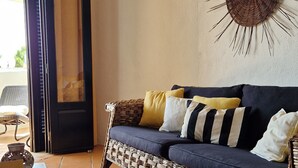 A living room with a dark blue sofa, yellow and white pillows, a woven coffee table, and a sunburst wall decoration. - Rustic apartment in Praia de Carvoeiro, Algarve (Carvoeiro)