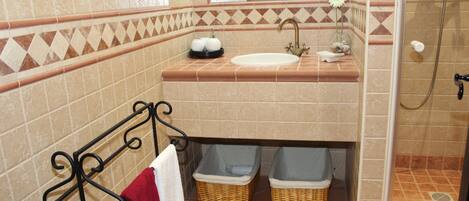 A bathroom with a sink, mirror, and shower. There are two baskets under the sink and a red towel hanging on a rack.