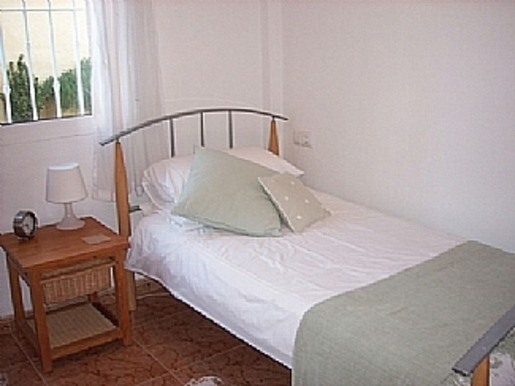 A single bed with a metal headboard, a bedside table with a lamp, and a window with curtains.