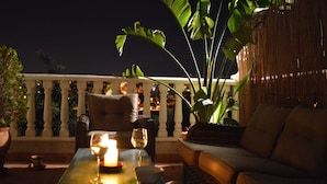 Een balkon met een bank, een tafel met een kaars en een potplant.