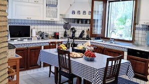 Une cuisine avec des meubles blancs, un pare-feu en carreaux, un lustre et une table à manger recouverte d’une nappe à carreaux.