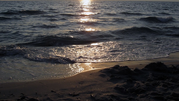 Une plage avec des vagues et le soleil qui se reflète sur l’eau.