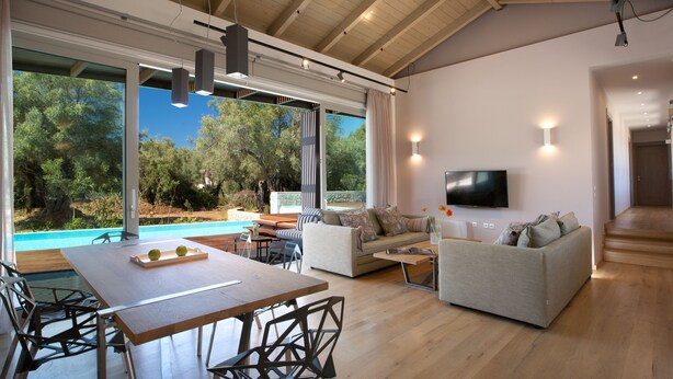 A spacious living area with a wooden dining table, sofas, and a TV mounted on the wall. - Kozanitis Brand New Exclusive Villa With Private Pool (Agrikies Villas) (Lefkada)