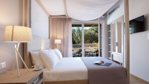 A hotel room with a large bed, a bedside table with a lamp, a TV mounted on the wall, and a balcony with outdoor seating. - Kozanitis Brand New Exclusive Villa With Private Pool (Agrikies Villas) (Lefkada)