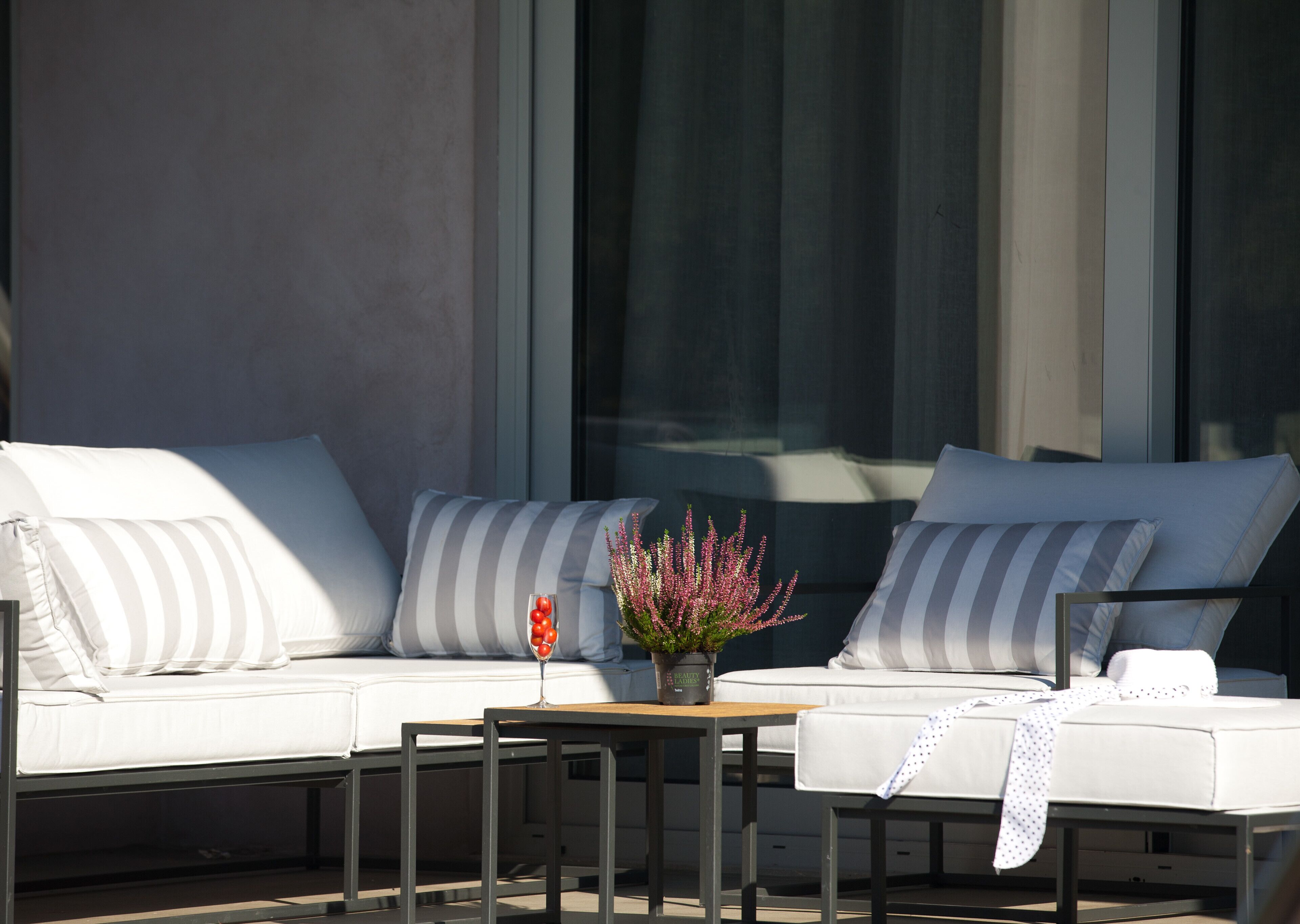 A modern outdoor seating area with a sofa and a small table, a potted plant, and a glass of red wine.