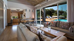 A spacious living area with a large sofa, a dining table, and a view of a swimming pool. - Kozanitis Brand New Exclusive Villa With Private Pool (Agrikies Villas) (Lefkada)