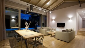 A modern living room with a wooden dining table, two sofas, and a TV mounted on the wall. - Kozanitis Brand New Exclusive Villa With Private Pool (Agrikies Villas) (Lefkada)