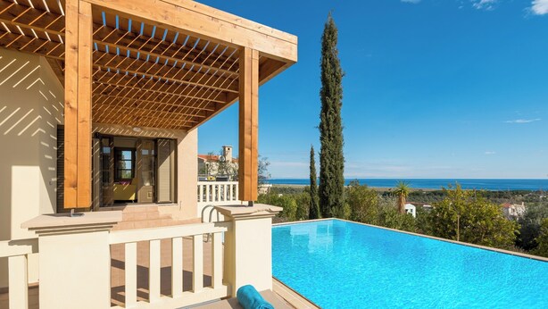 Un espace aménagé au bord de la piscine, doté d’une pergola, d’une terrasse en bois et offrant une vue sur la mer.