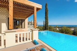 Un espace aménagé au bord de la piscine, doté d’une pergola, d’une terrasse en bois et offrant une vue sur la mer.