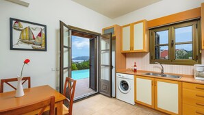 Une cuisine compacte équipée d’un lave-linge, un coin repas avec une table et des chaises, et une vue sur l’extérieur.