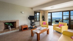 Un salon avec une cheminée, un téléviseur, un canapé jaune et un balcon avec vue.