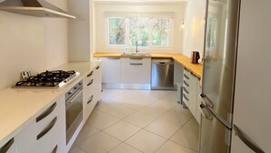 A modern kitchen with white cabinetry, stainless steel appliances, and a large window providing natural light. - Private villa with mature gardens, 2 minutes walk from sandy beach. (sant lluis)