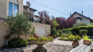 Une cour avec un banc blanc, des plantes en pot et une maison avec un garage.