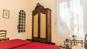Une chambre avec deux lits, une armoire en bois, une petite table sur laquelle se trouve un saladier rempli de fruits, et une chaise.