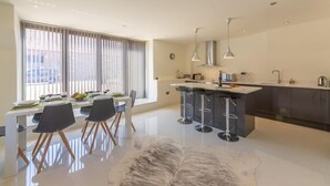 A modern kitchen with a central island, bar stools, and a dining area with a white table and chairs. - Tun House, Letheringsett, Norfolk (Letheringsett)