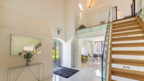 A spacious, modern interior with a polished floor, a glass staircase, and a dining area visible through an open archway. - Tun House, Letheringsett, Norfolk (Letheringsett)