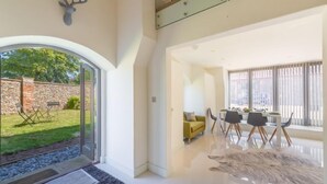 A modern interior with a glass door leading to a garden, a dining area with a yellow sofa, and a large fur rug. - Tun House, Letheringsett, Norfolk (Letheringsett)