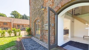 A modern building with a stone facade, large glass doors leading to an interior space, and a gravel pathway. - Tun House, Letheringsett, Norfolk (Letheringsett)