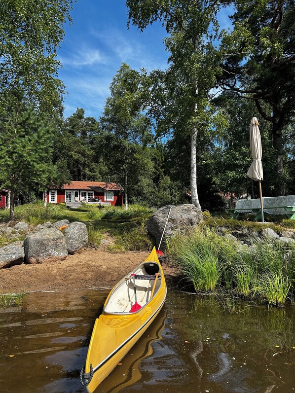 A yellow canoe tied to a rock near a house with a red roof. - For seasonal updates, follow Instagram account sjostuganinsmaland (Solberga)