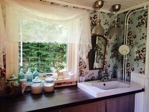 A bathroom with a large window, floral wallpaper, a white sink, and a mirror. - For seasonal updates, follow Instagram account sjostuganinsmaland (Solberga)