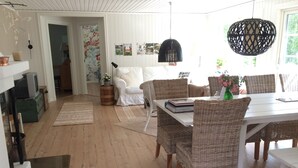 Zona pranzo con tavolo bianco, sedie in vimini e lampadario nero.