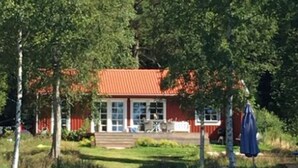 Una casa con tetto rosso, un portico e uno stagno di fronte.
