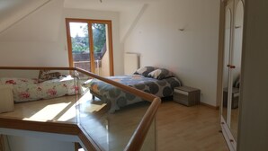 Ein Schlafzimmer mit einem Bett, einem kleinen Nachttisch, einem Holztisch und einem Fenster mit Blick ins Grüne.