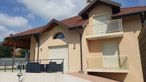 Ein zweistöckiges Gebäude mit rotem Ziegeldach, beige farbenen Außenwänden und einem überdachten Außenbereich mit Tischen und Stühlen.