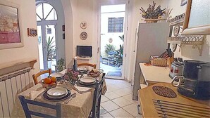 A dining area with a table set for four, a television in the background, and a kitchen area with a refrigerator and stove. - FLORENCE HISTORIC CENTER, APARTMENT WITH PRIVATE COURTYARD, WI-FI and AC (firenze)