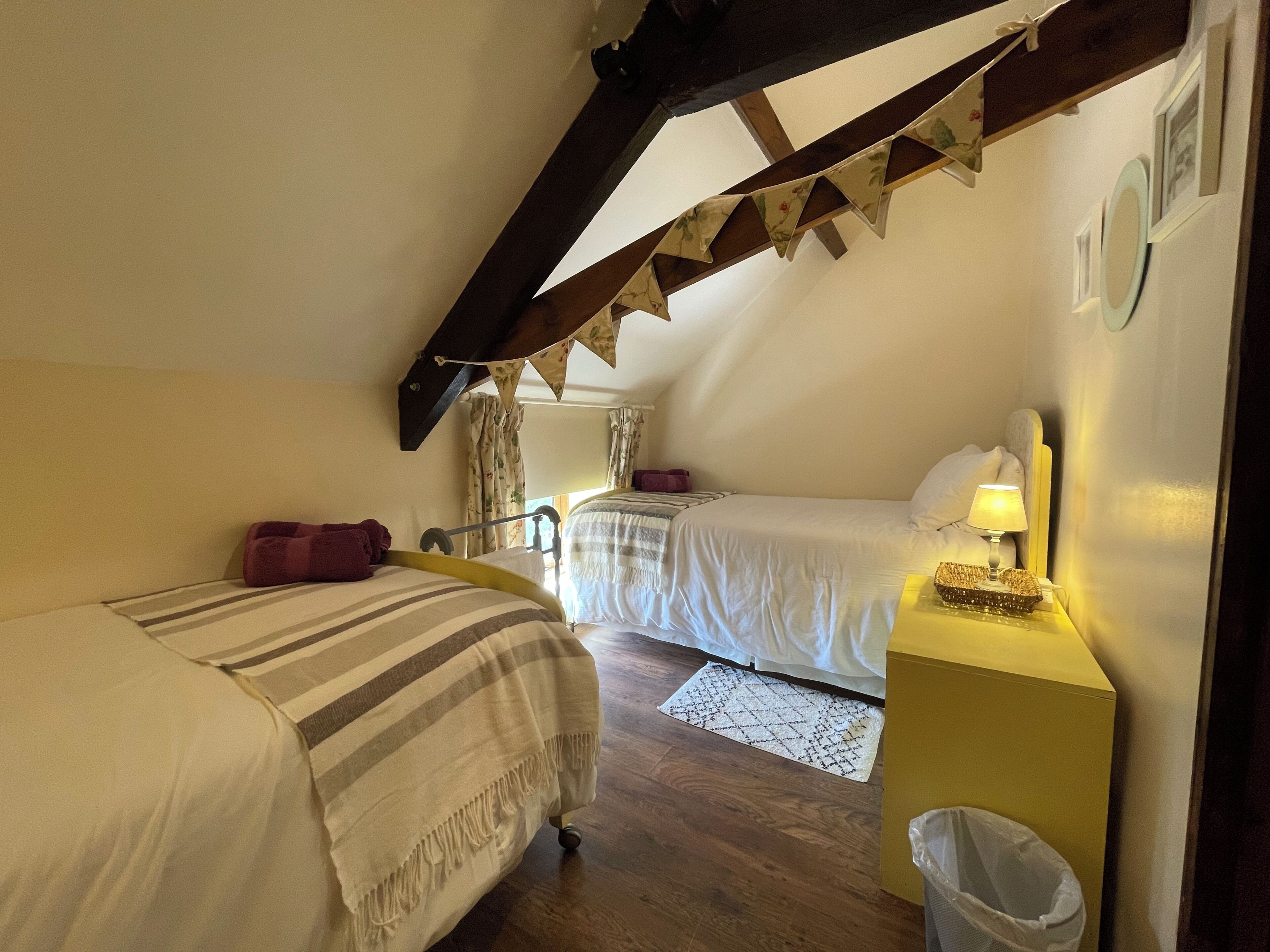 A bedroom with two beds, a wooden ceiling, and a nightstand with a lamp.