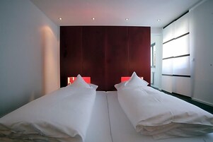 Un dormitorio moderno con dos camas, un cabecero oscuro y un ventanal grande.