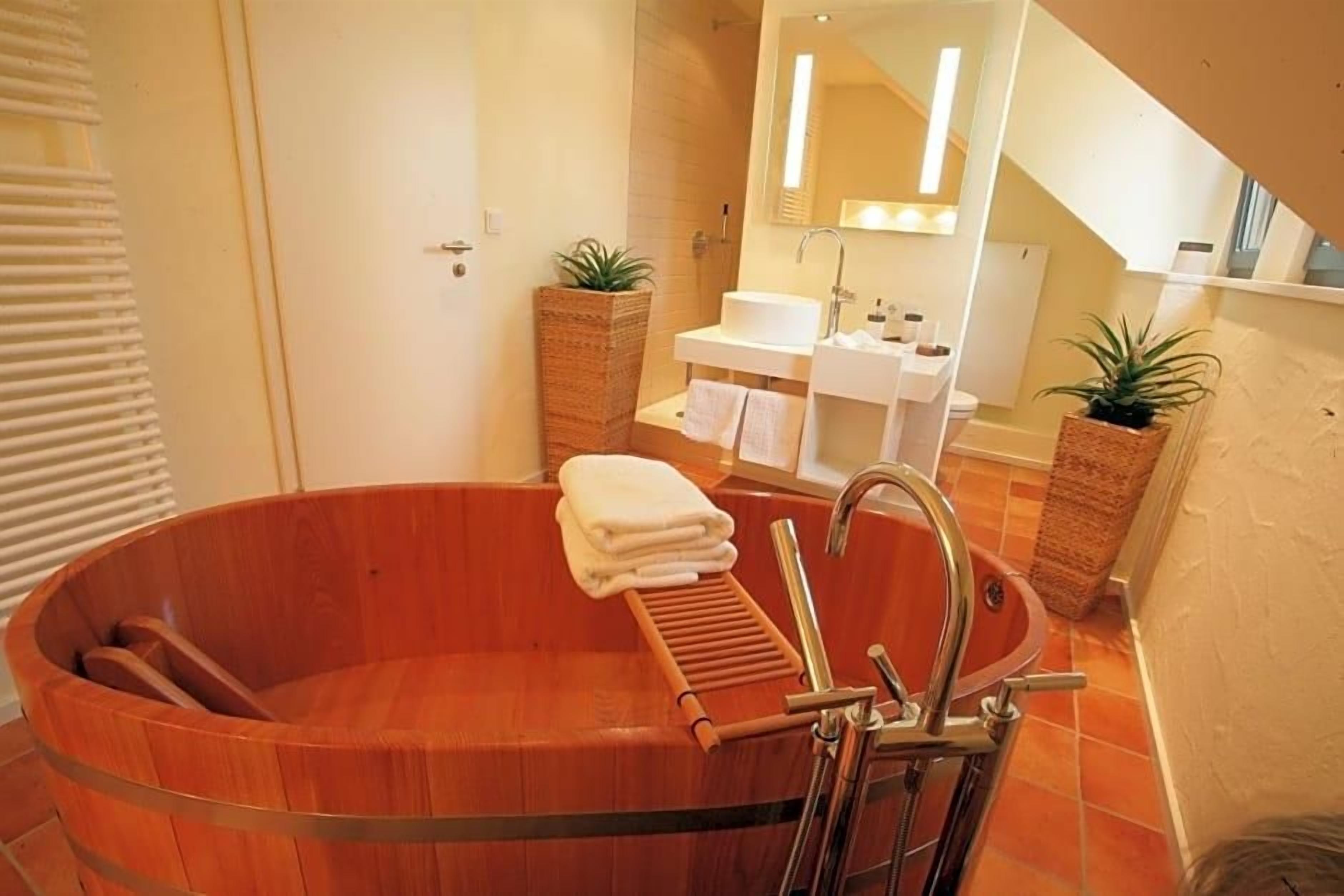 A bathroom with a wooden bathtub, a sink, and two potted plants.