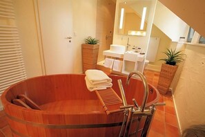 A bathroom with a wooden bathtub, a sink, and two potted plants. - Vinotel Augustin (Sulzfeld am Main)