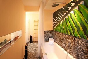 Un baño con bañera, ducha y un muro decorativo con motivos de hojas.