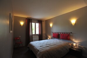 Een slaapkamer met een bed, een stoel, twee nachtkastjes met lampen en een raam met gordijnen.