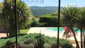 Eine Terrasse im Freien mit Tisch und Stühlen, mit Blick auf einen Pool und üppiges Grün.