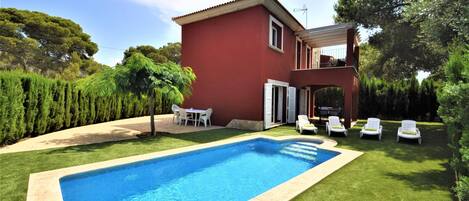 A red house with a swimming pool and outdoor seating.