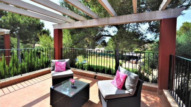 Un espace extérieur aménagé, abrité et doté de deux canapés et d’une table, entouré d’une rambarde en métal et d’arbres.