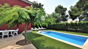 Une piscine dont le bord est revêtu de carrelage, entourée d’une pelouse bien entretenue et bordée d’une rangée de chaises longues blanches.
