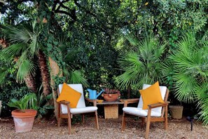 A garden setting with two white chairs, a wooden table, and a potted plant.