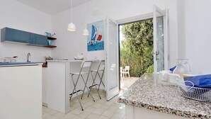 A modern kitchen with a central island, white cabinetry, and a dining area with chairs.