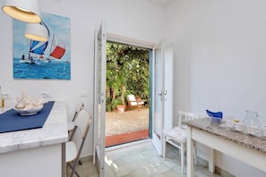 Une cuisine moderne avec un plan de travail en marbre, un tableau représentant des voiliers et une vue sur un jardin, visible à travers une porte ouverte.
