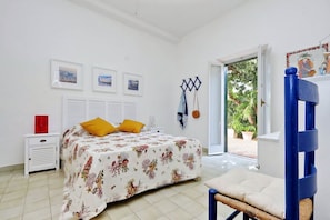 A bedroom with a bed, a nightstand, a chair, a window, and a door leading outside.